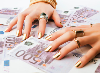 hands of rich woman with golden manicure and many jewelry rings on cash euros close up
