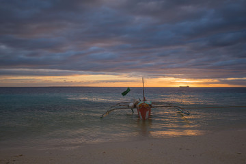 Fototapeta na wymiar outrigger fisher boat at the beach on the white sand, in a tranquil summer sunset dusk background photo