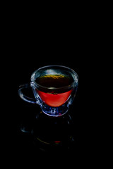 Tea in a transparent mug on a black background with reflection
