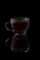 Tea in a transparent mug on a black background with reflection