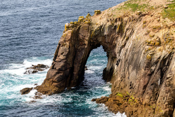 Obraz premium A wild and beautiful rock arche at Land’s End, Cornwall, United Kingdom, with blue water