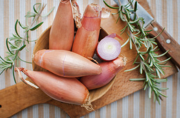 Close-up of shallots in a wooden bowl with fresh rosemary on cutting board, top view