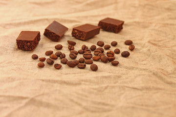 Chocolate cubes with coffee beans on a linen texture background.