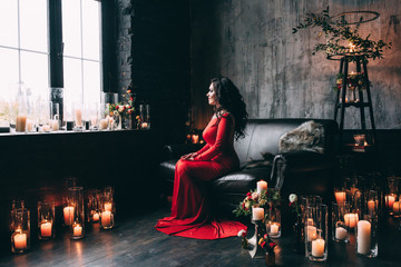 Brunette with beautiful hair in a red dress on a black sofa.