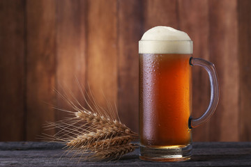 Mug of beer with wheatears on wood background