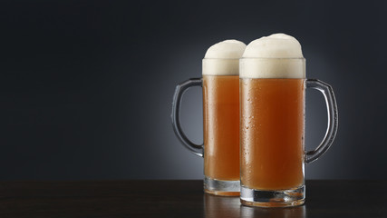 Two frosty mugs of beer on gradient gray