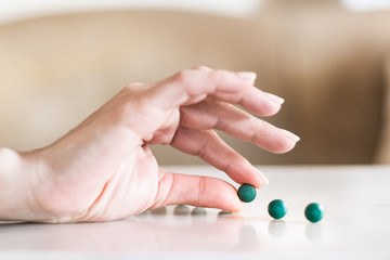 Obraz na płótnie Canvas Female hand holding a spirulina pill next to pills on a table.