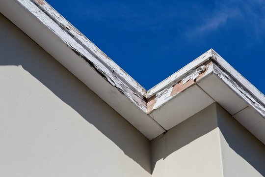 Roof repair and maintenance concept image consisting of old rotting fascia boards and a blue sky background. 