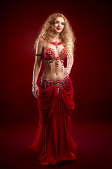 Fototapeta premium Beautiful young girl dancer with white curly long hair in a red costume with rhinestones, on a red background