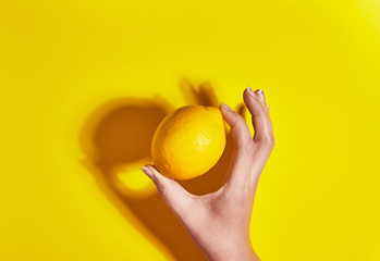Lemon in hand on yellow background. Flat lay, top view, copy space . Food concept.