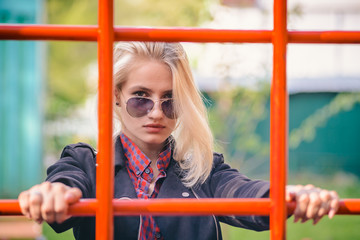 Obraz premium Cool girl in sunglasses looking through the net on the Playground in the Park for a walk.