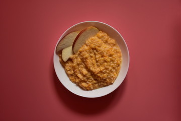 Porridge from millet with pumpkin in white glass plate on the pink background closeup.