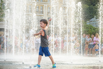 excited boy having fun between water jets, in fountain. Summer in the city