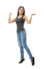 Obraz premium Young smiling woman in sleeveless gray top and blue jeans standing on tiptoes with arms bent and raised to sides isolated on white background.