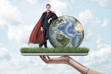 Businessman in mask and cape standing and resting one elbow on Earth globe, on top of digital...