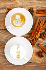 Two cups of coffee, cinnamon and anise on wooden backg