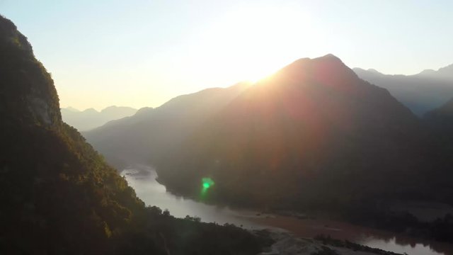 Aerial: flying over Nam Ou River Nong Khiaw Muang Ngoi Laos, sunset dramatic sky, scenic mountain landscape, famous travel destination in South East Asia.
