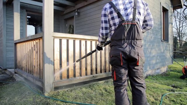 Man cleaning terrace with a power washer - high water pressure cleaner on wooden terrace railing