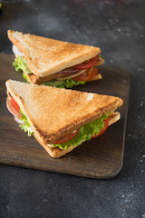 Two sandwiches with bacon,tomato, onion, salad on chopping board and dark. Close up.