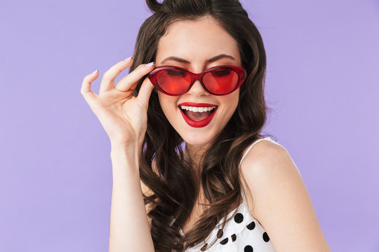 Portrait of seductive pin-up woman 20s in vintage polka dot dress and retro sunglasses smiling at camera