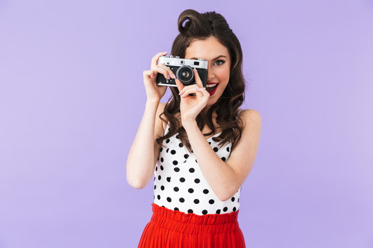 Portrait of beautiful pin-up woman 20s in vintage polka dot dress smiling while holding retro photo camera