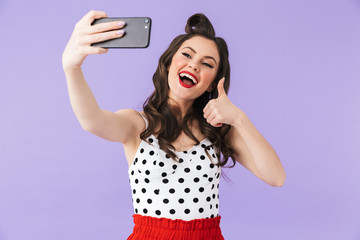 Naklejka premium Photo of beautiful pin-up woman 20s in vintage polka dot dress holding and taking selfie photo on black smartphone