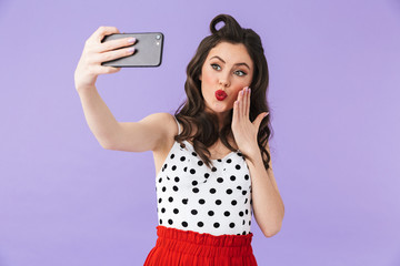 Photo of gorgeous pin-up woman 20s in vintage polka dot dress holding and taking selfie photo on black smartphone