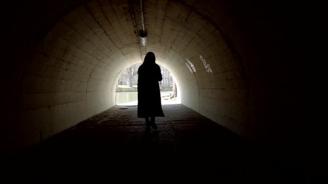 lonely woman is walking through dark tunnel in old city, back view of her silhouette