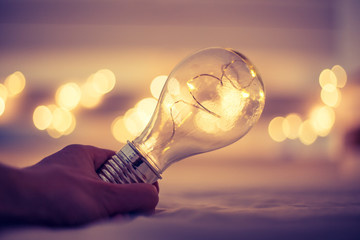 Ideas and innovation: Light bulb with LEDs is lying in the bed, hands touching. Spot lights in the blurry background.