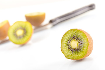 Green fresh kiwi fruit cut into half and knife on a white background