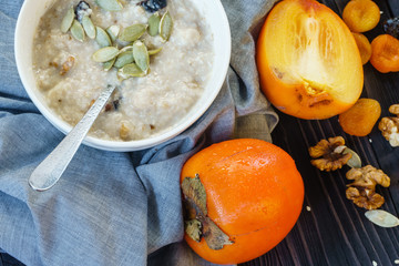 Oatmeal with Persimmon, Prune, Dried Apricots, Walnut, Pumpkin Seeds and Sesame on a Black Wooden Table Top View Copy Space Background