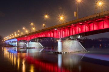 White and red illuminated at Slasko-Dabrowski bridge over Vistula River at night in Warsaw, Poland.