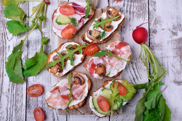 Bruschetta assortment with cream cheese, champignons, pancetta meat, vegetables and greenery
