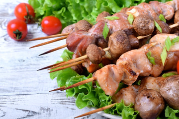 Grilled shashlik of pork, chicken and champignons on wooden skewers against the light background