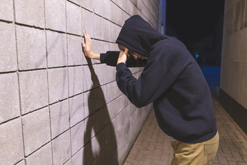 Hooded teenager leaning against a brick wall in an alleyway. He is suffering from depression.