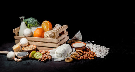 Foods rich in calcium such as sardines, bean, dried figs, almonds, hazelnuts, parsley leaves, broccoli, italian cabbage, cheese, milk, yoghurt on dark background