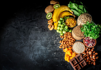 Assortment of high magnesium sources: bananas, nuts, oatmeal, buckwheat, peanuts, spinach chard, dark chocolate and sesame seeds on dark background