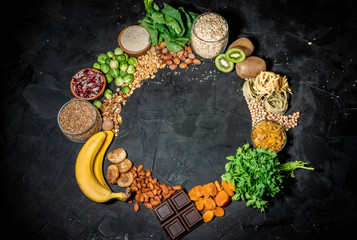 Assortment of high magnesium sources: bananas, nuts, oatmeal, buckwheat, peanuts, spinach chard, dark chocolate and sesame seeds on dark background