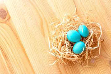 Three blue eggs in a nest on a light wooden background. Easter celebrate concept.