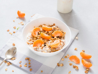 Healthy breakfast. Baked muesli with tropical fruits, fresh tangerines and yogurt on white background