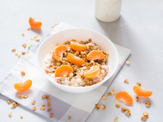 Healthy breakfast. Baked muesli with tropical fruits, fresh tangerines and yogurt on white background