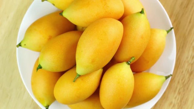 Top view of ripe Marian plum in a white plate on wooden table