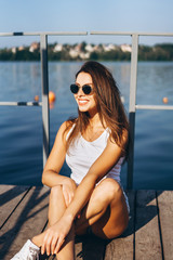 Cute young brunette girl relaxing on the pier near lake.