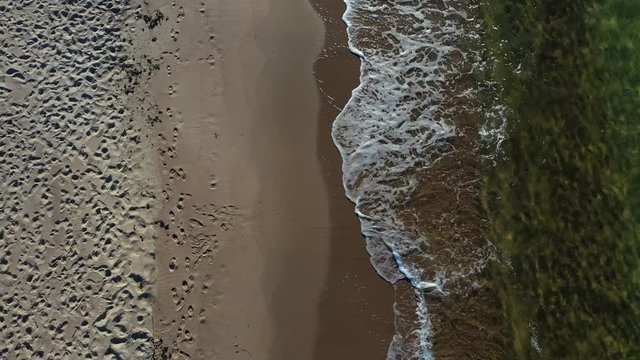 Drone shot, top view of the Beach of Preila, Curonian Spit, Lithuania, with waves crashing on the shore, on a sunny day with clouds