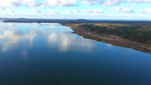 Drone shot of a small red light house with birds flying around, near Pervalka, Lithuania, near the coastline, in the calm sea with reflecting surface, on a bright sunny day