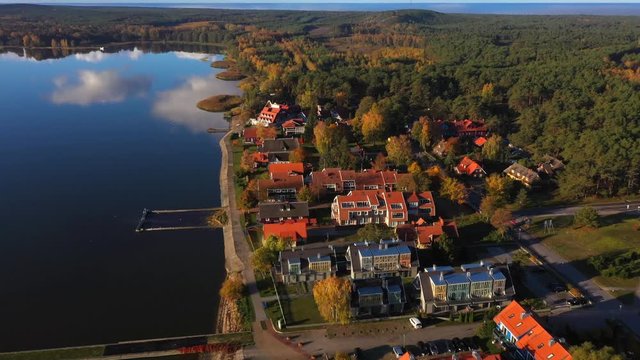 Drone shot of Pervalka, small village in Lithuania, surrounded by autumnal forest, near the coastline and the calm sea, reflecting white clouds on the surface, on a bright sunny day