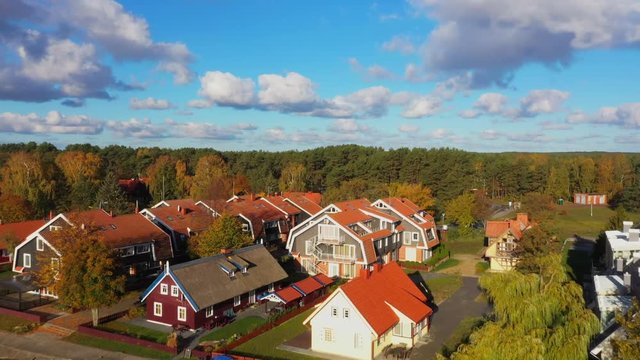 Forward rising drone shot of Pervalka, small village in Lithuania, surrounded by autumnal forest, near the coastline and the calm sea, reflecting white clouds on the surface, on a bright sunny day