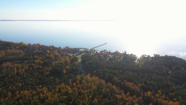 Drone shot of Pervalka, small village in Lithuania, surrounded by autumnal forest, near the coastline and the calm sea with reflecting surface, on a bright sunny day