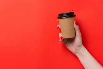 Hand holding paper cup of coffee on red background.