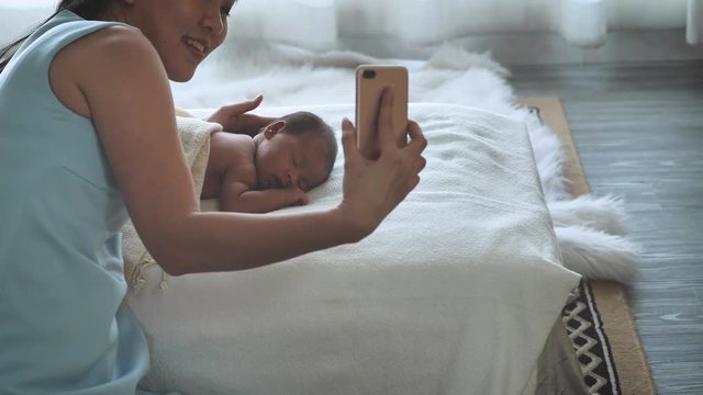 Mother Asian and newborn baby talking to each other through a video call n a smartphone